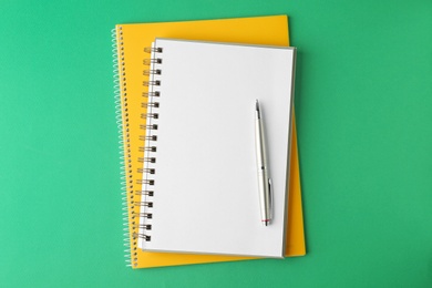 Photo of Notebooks and pen on green background, top view