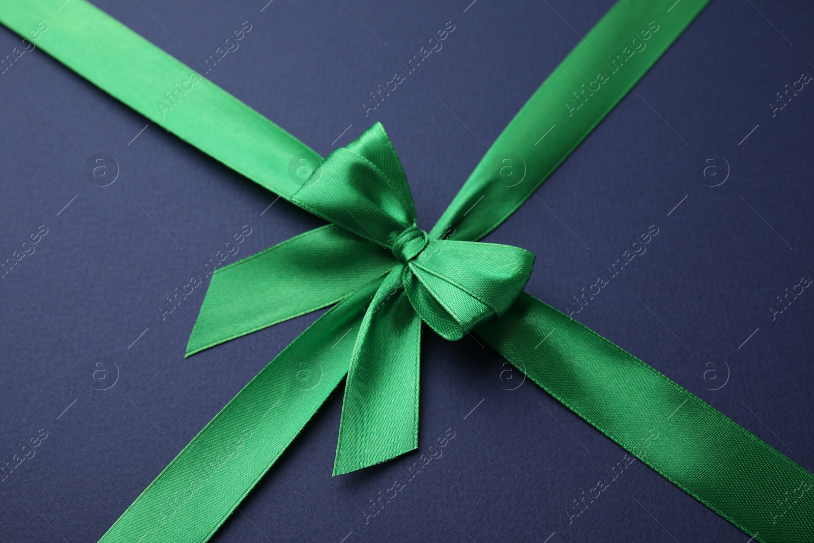 Photo of Green satin ribbon with bow on blue background