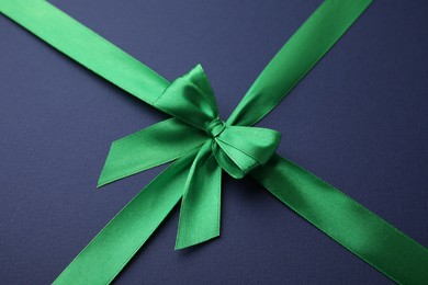 Photo of Green satin ribbon with bow on blue background