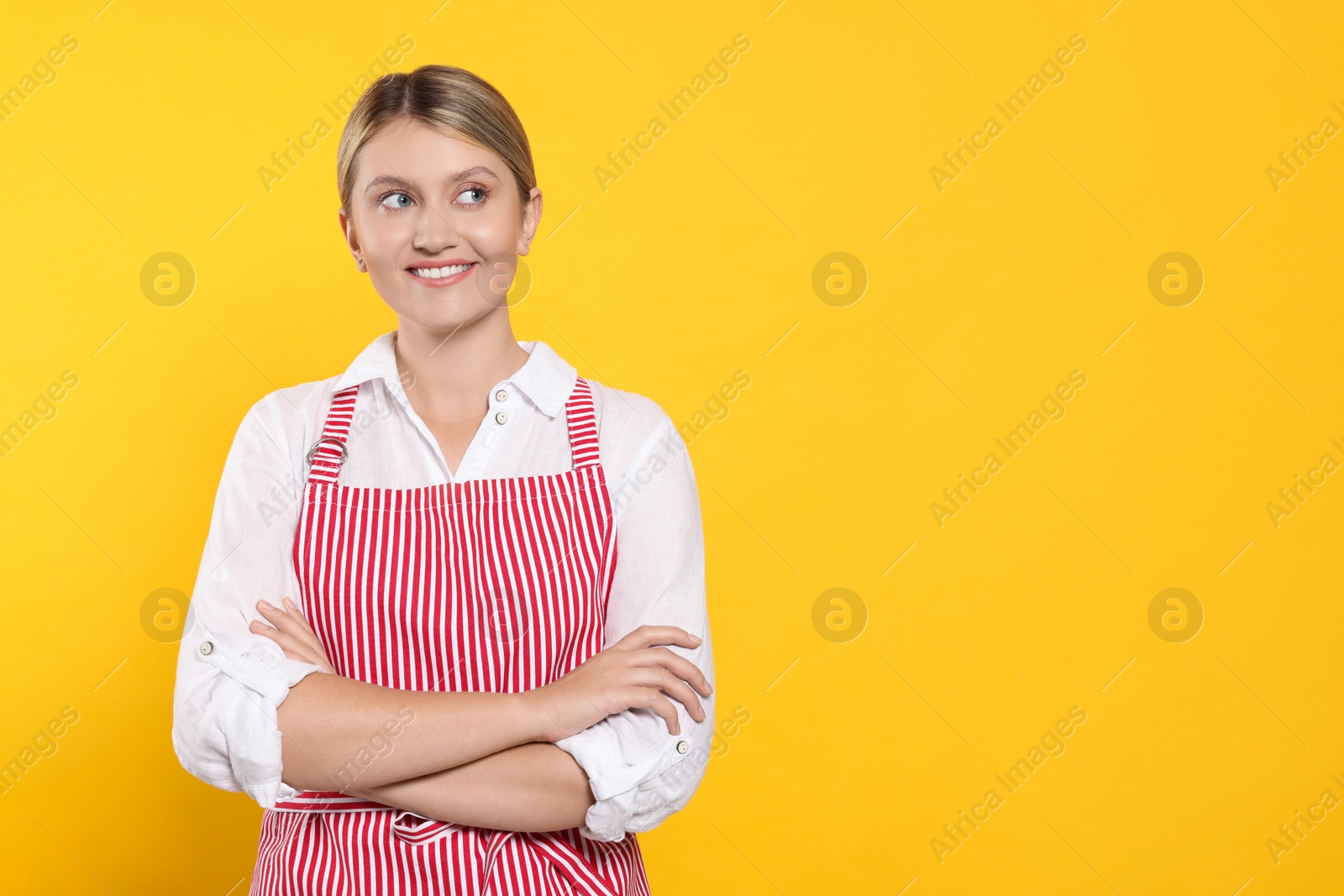 Photo of Beautiful young woman in clean striped apron on orange background. Space for text