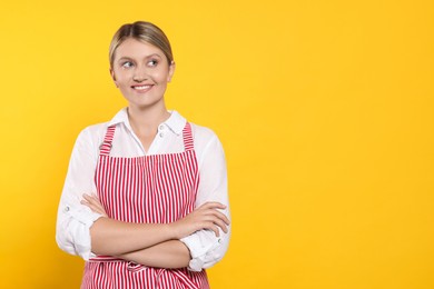Photo of Beautiful young woman in clean striped apron on orange background. Space for text