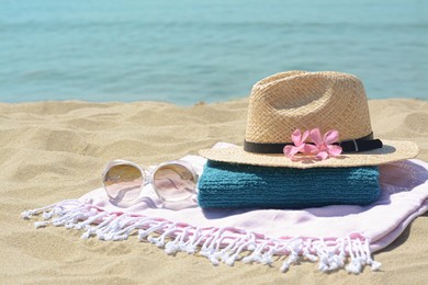 Stylish beach accessories and flowers on sand near sea