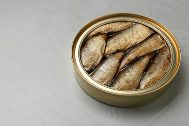 Photo of Open tin can of sprats on light grey table, closeup. Space for text