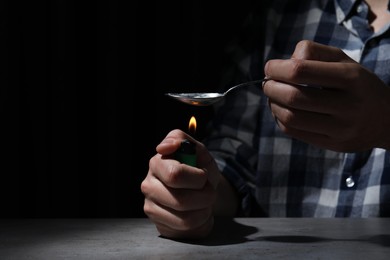 Man preparing drugs with spoon and lighter at grey table, closeup