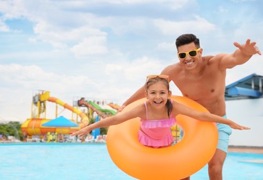 Photo of Father and daughter with inflatable ring near pool in water park, space for text. Family vacation