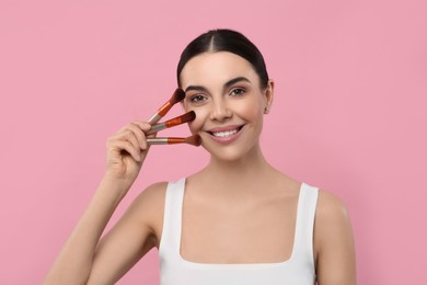 Photo of Happy woman with different makeup brushes on pink background