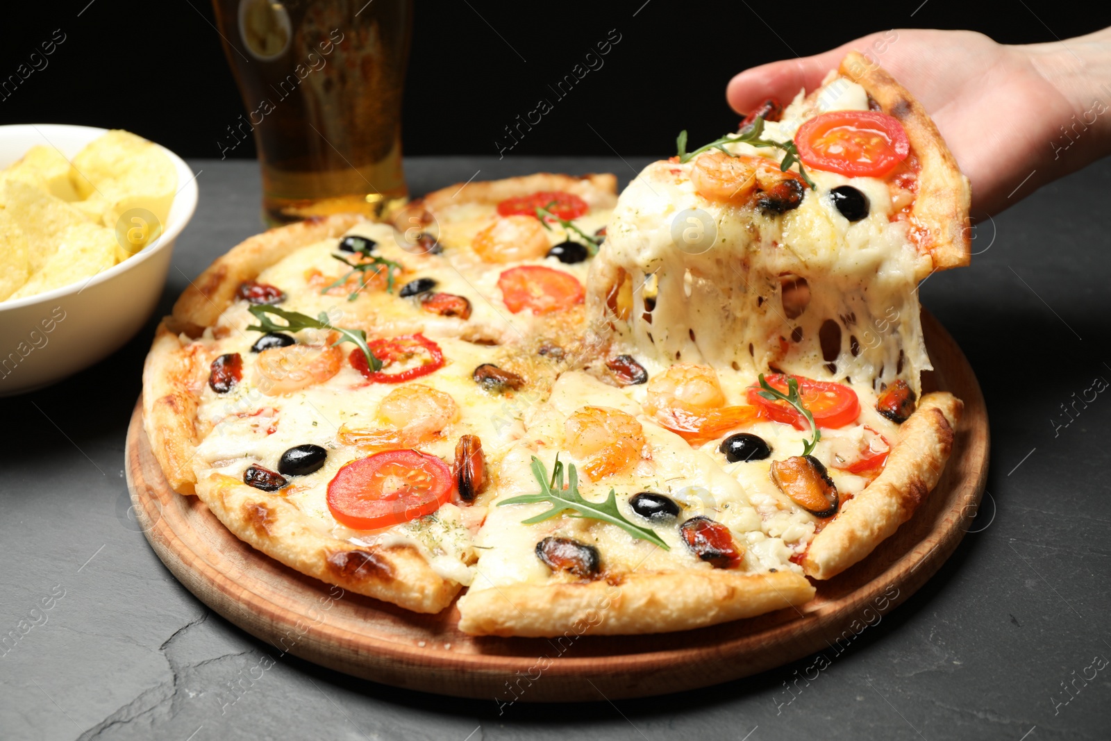 Photo of Woman taking slice of cheese pizza with seafood at black table, closeup