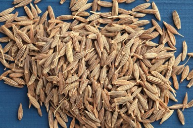 Photo of Pile of caraway seeds on blue wooden table, top view