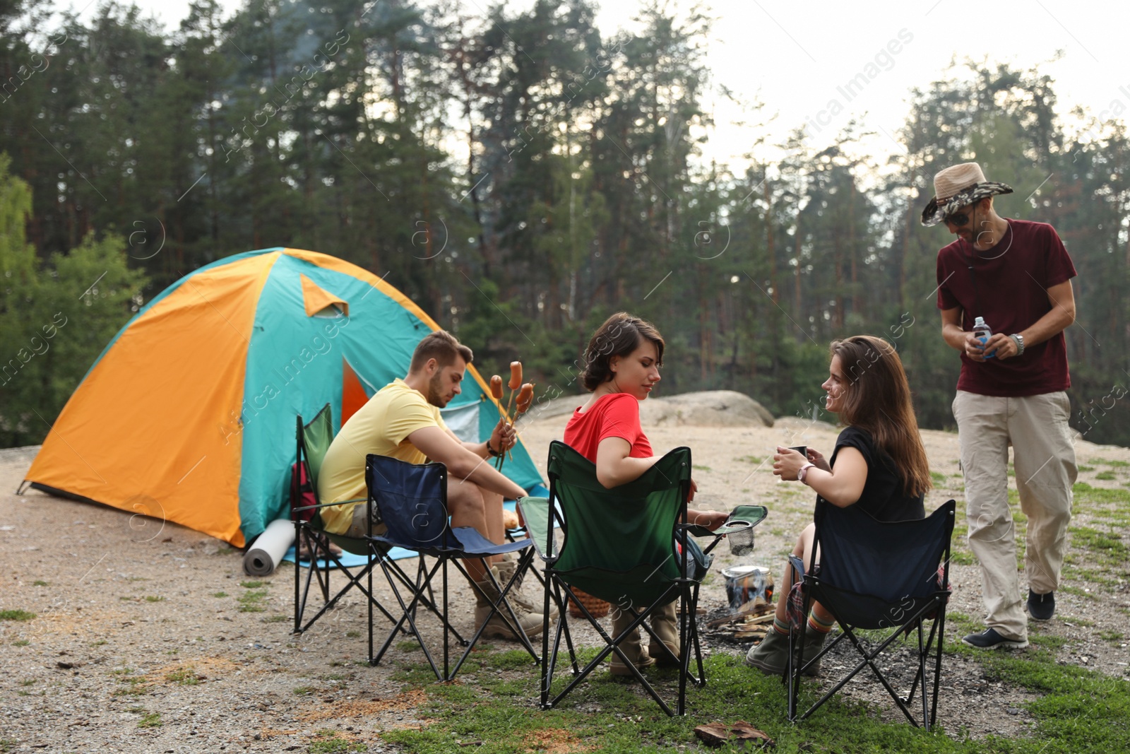 Photo of Young people having lunch with sausages near camping tent outdoors