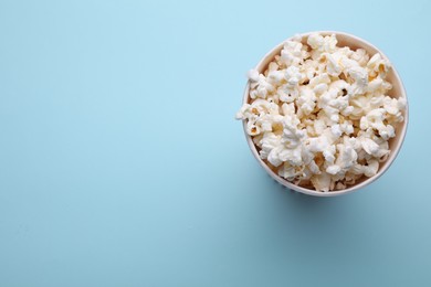 Paper bucket with delicious popcorn on light blue background, top view. Space for text