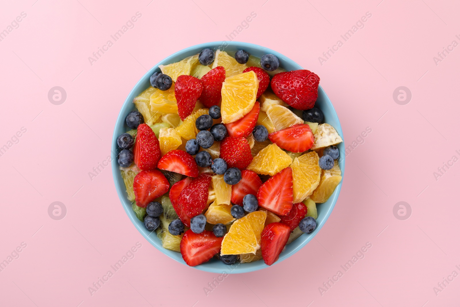 Photo of Yummy fruit salad in bowl on pink background, top view