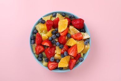 Yummy fruit salad in bowl on pink background, top view