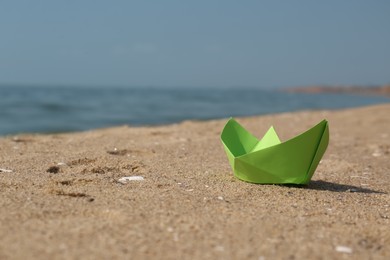 Photo of Light green paper boat on sandy beach near sea, space for text