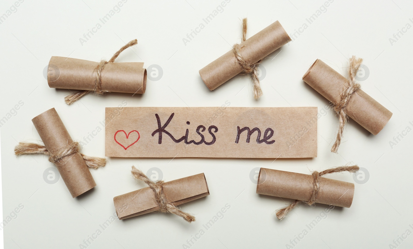 Photo of Card with phrase Kiss Me near rolled papers on beige background. flat lay