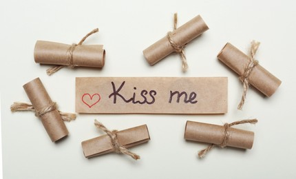 Card with phrase Kiss Me near rolled papers on beige background. flat lay