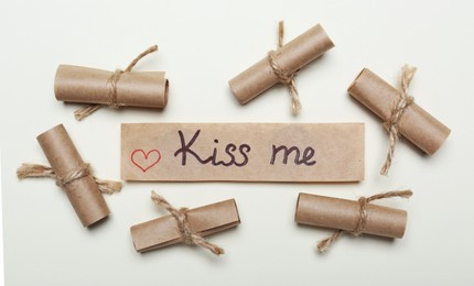 Photo of Card with phrase Kiss Me near rolled papers on beige background. flat lay