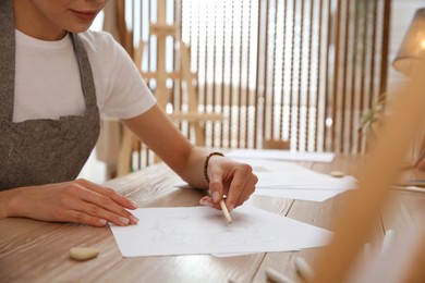 Photo of Young woman drawing male portrait at table indoors, closeup