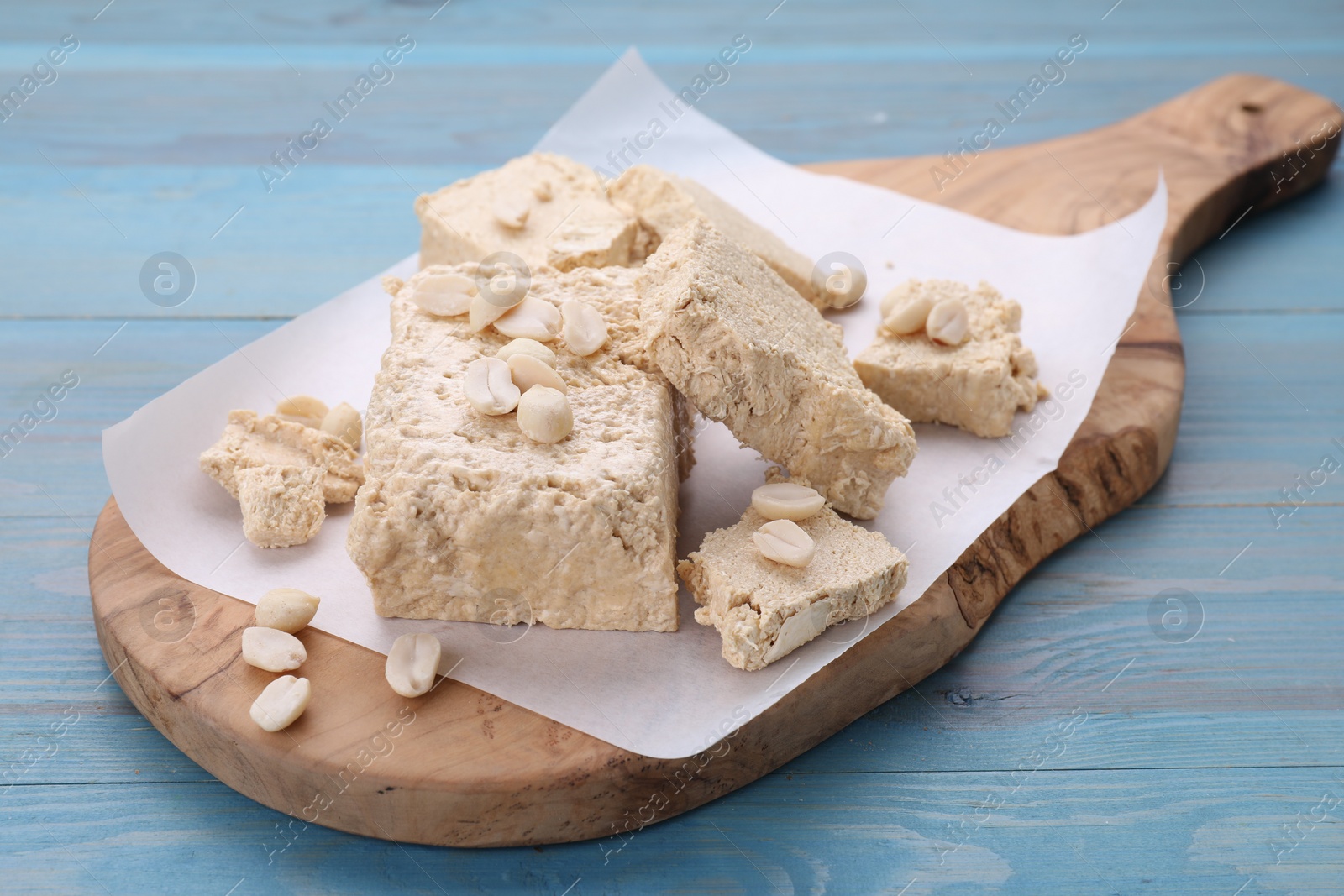 Photo of Pieces of tasty halva and peanuts on light blue wooden table
