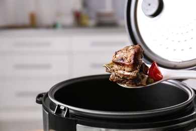 Photo of Spoon with meat and vegetables over modern multi cooker in kitchen, closeup. Space for text