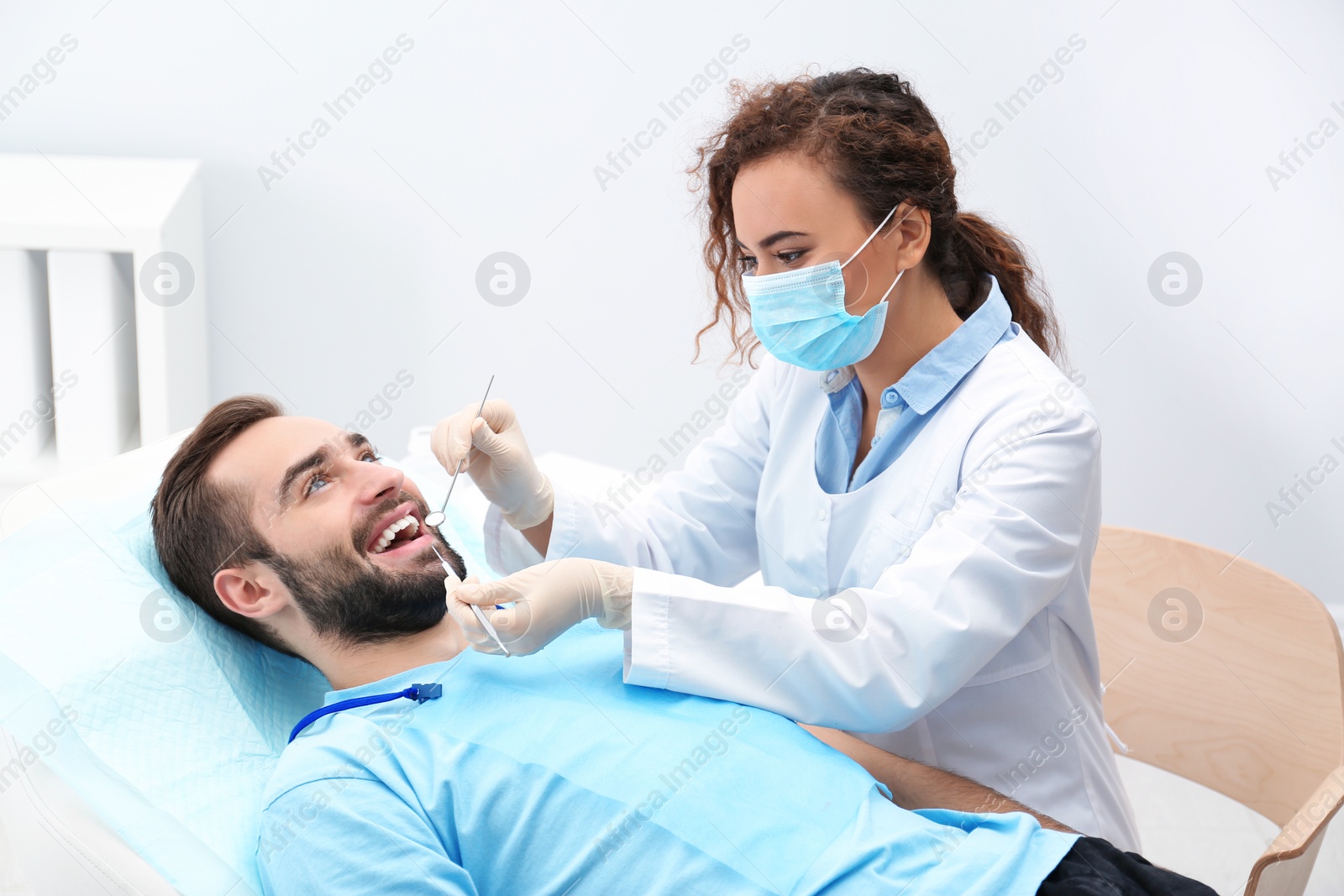 Photo of Dentist examining young man's teeth with mirror and probe in hospital