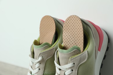 Photo of Orthopedic insoles in shoes near white wall, closeup. Space for text