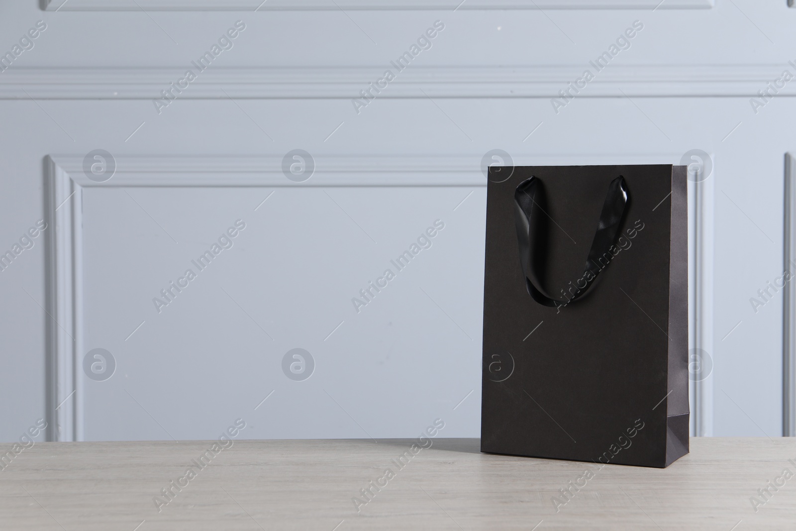 Photo of Black paper bag on wooden table against light grey wall, space for text