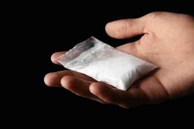 Photo of Drug dealer holding bag with cocaine on black background, closeup
