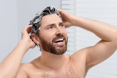 Photo of Happy man washing his hair with shampoo in shower