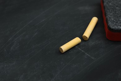 Pieces of yellow chalk and duster on black board, closeup. Space for text