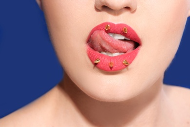 Photo of Beautiful young model with decorative spikes on lips against color background