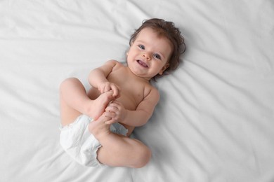 Cute baby in diaper lying on bed, top view