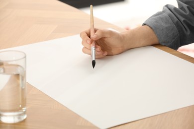 Photo of Man painting with watercolor on blank paper at wooden table, closeup