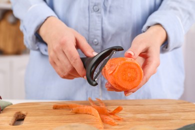 Photo of Woman peeling fresh carrot at table indoors, closeup