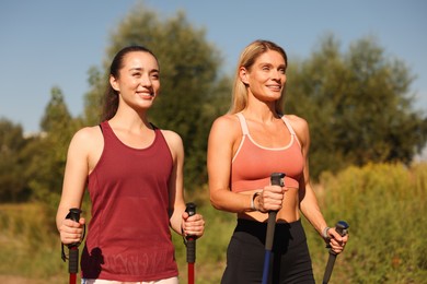 Happy women practicing Nordic walking with poles outdoors on sunny day