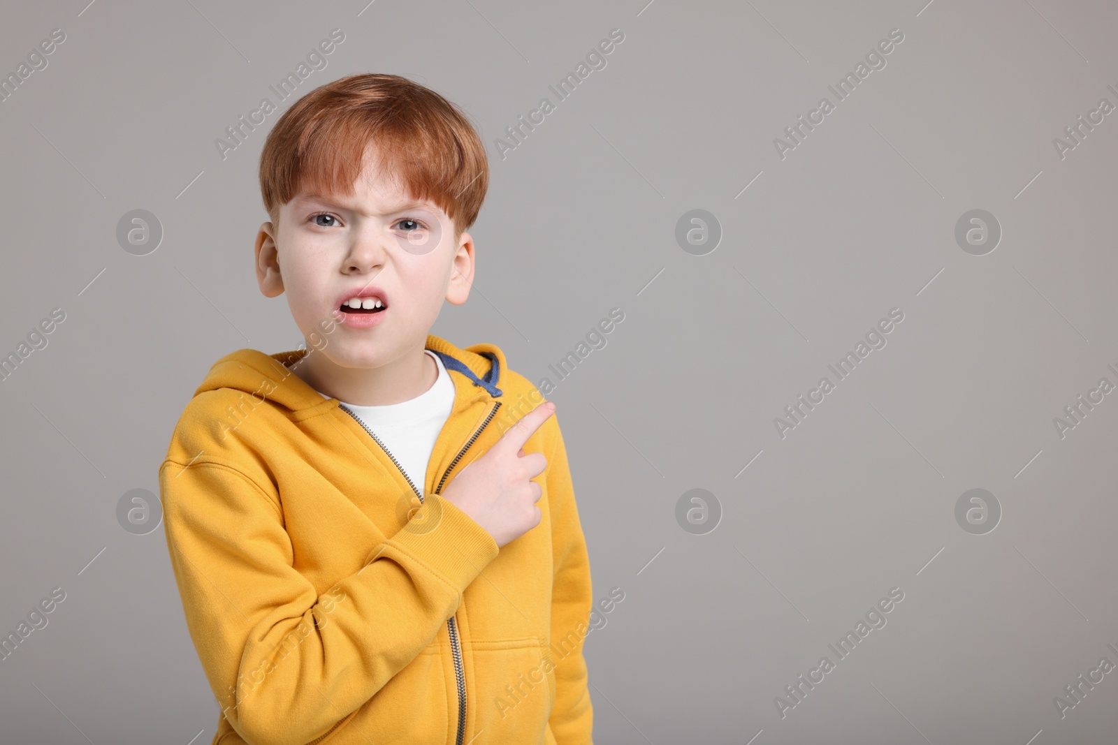 Photo of Surprised little boy pointing at something on grey background, space for text