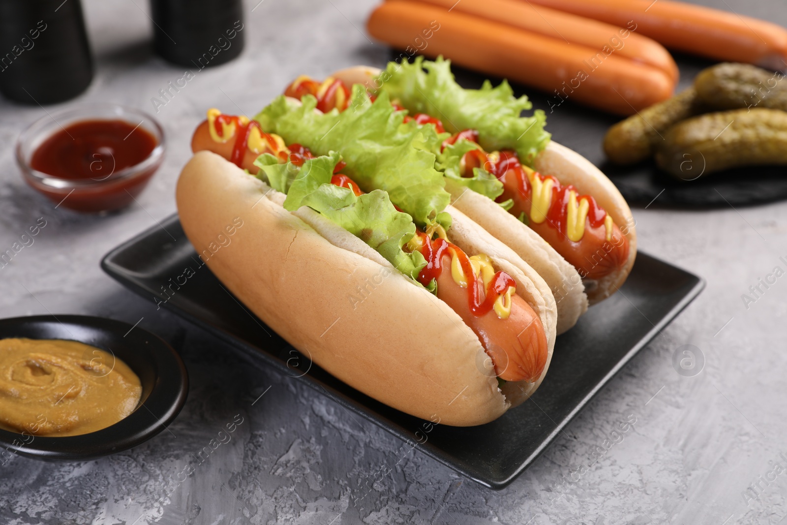 Photo of Tasty hot dogs with lettuce, ketchup and mustard on grey textured table