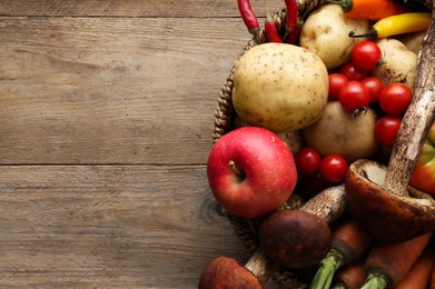 Basket with different fresh ripe vegetables and fruits on wooden table, top view. Space for text