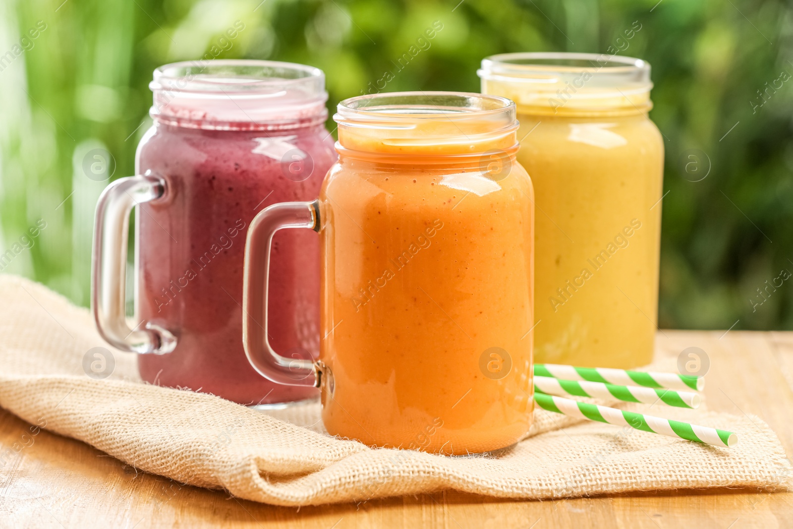 Photo of Different delicious smoothies in mason jars on wooden table against blurred background