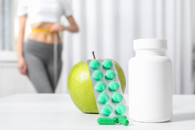 Weight loss pills with apple on table and woman measuring waist indoors