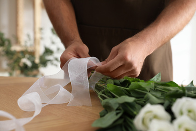 Florist making beautiful bouquet at table in workshop, closeup