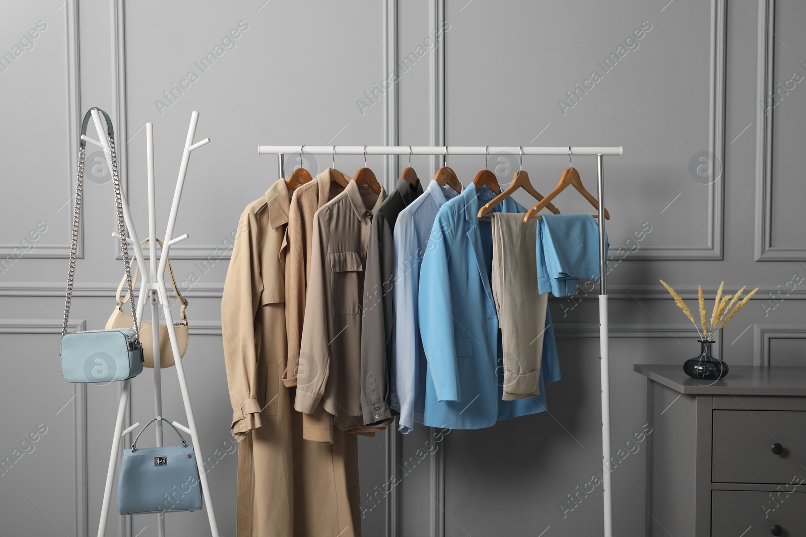 Photo of Rack with different stylish women`s clothes and bags near grey wall