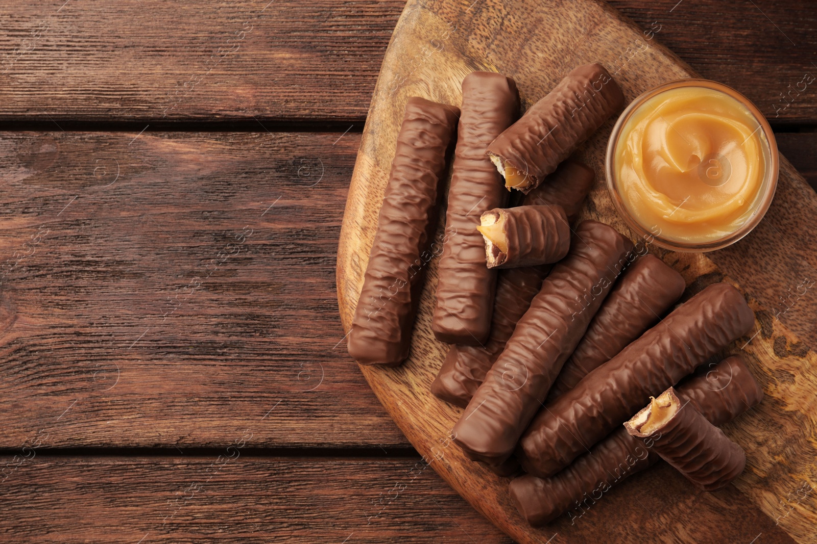 Photo of Sweet tasty chocolate bars with caramel on wooden table, top view. Space for text