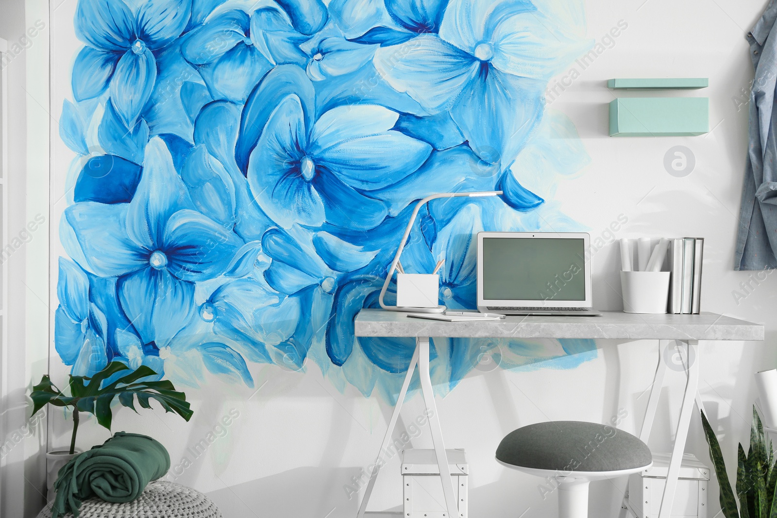 Photo of Stylish workplace with blue flowers painted on wall. Floral pattern in living room interior