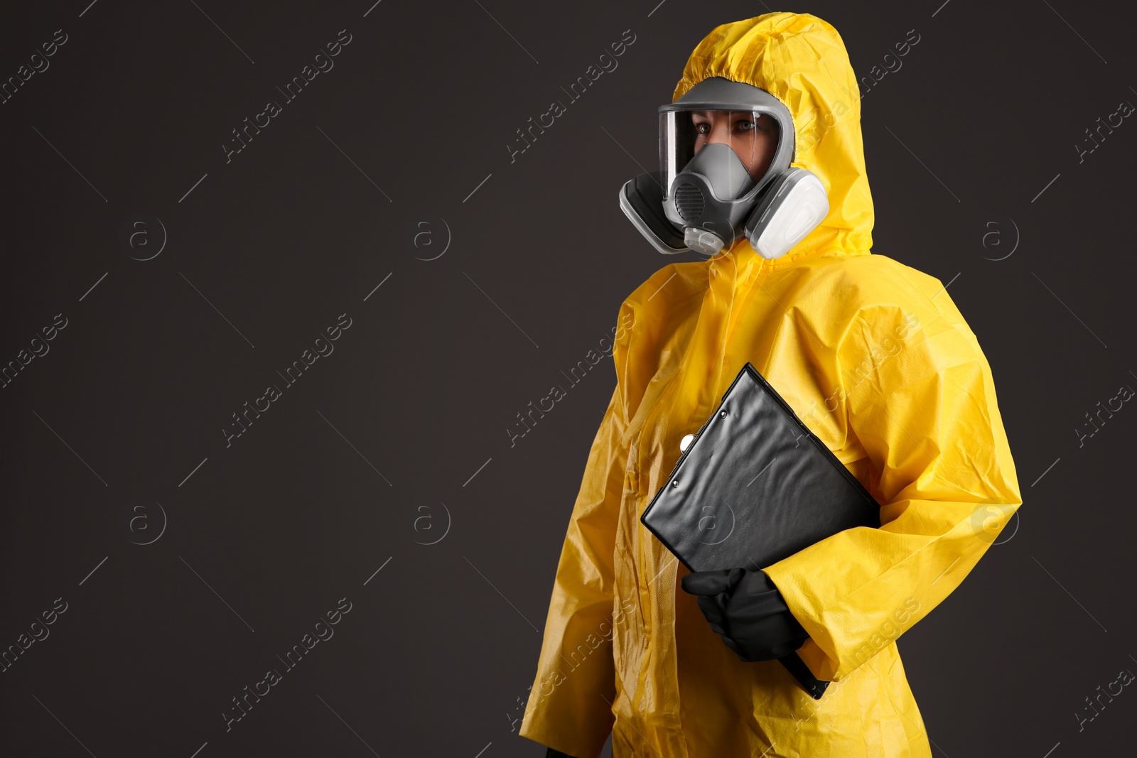 Photo of Woman in chemical protective suit holding clipboard on grey background, space for text. Virus research