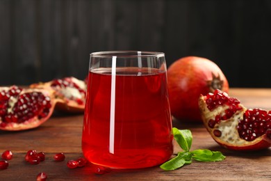 Photo of Tasty pomegranate juice in glass and fresh fruits on wooden table, closeup