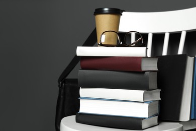 Stack of different books, paper cup and glasses on white chair. Space for text