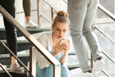 Young woman with smartphone sitting on stairs. Alone among people