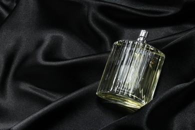 Photo of Luxury men's perfume in bottle on black satin fabric, above view. Space for text