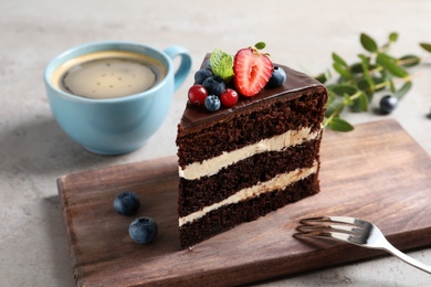 Wooden board with chocolate sponge berry cake and cup of coffee on grey background