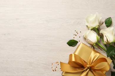 Photo of Golden gift box and beautiful roses on wooden background, flat lay. Space for text